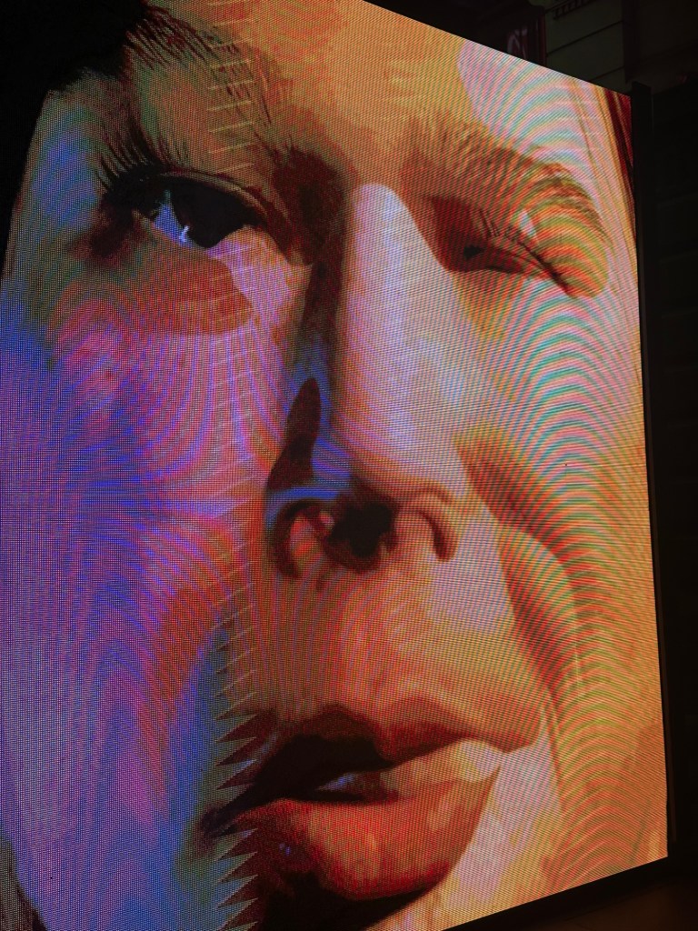 Close-up of a digitally rendered face singing on the outdoor screen at Melbourne Town Hall.